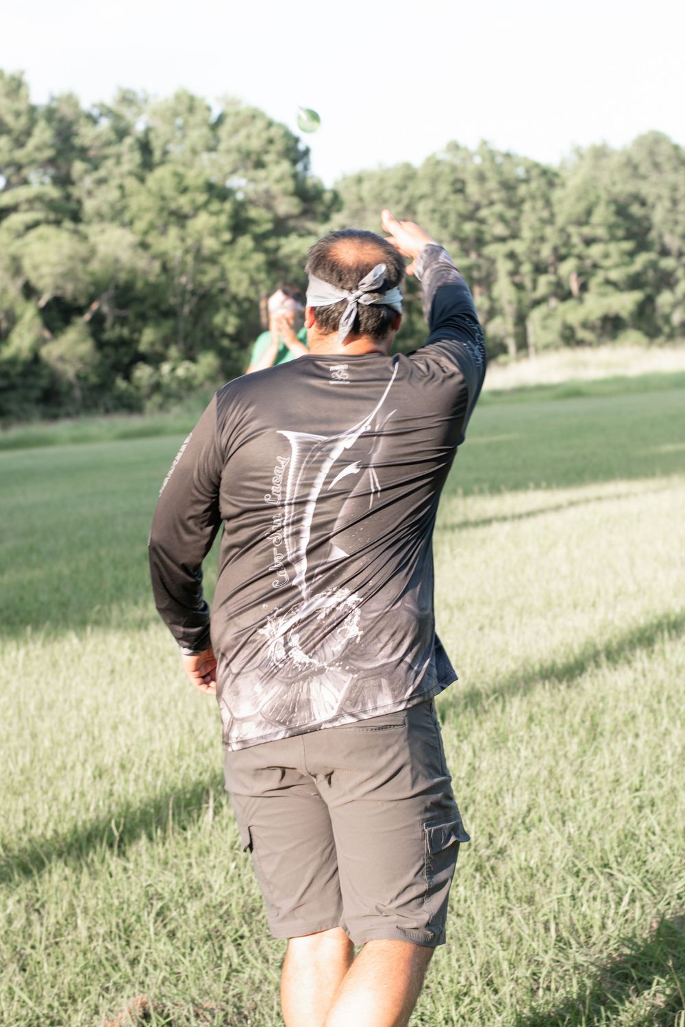 Person in dark athletic wear photographing in a green summer field.