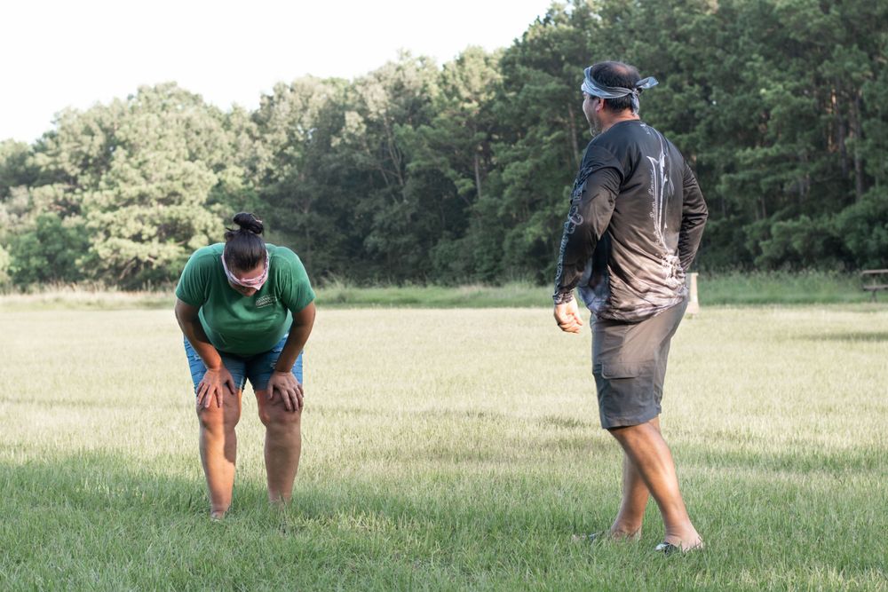 Two people engaged in an outdoor activity on a grass lawn near woods.