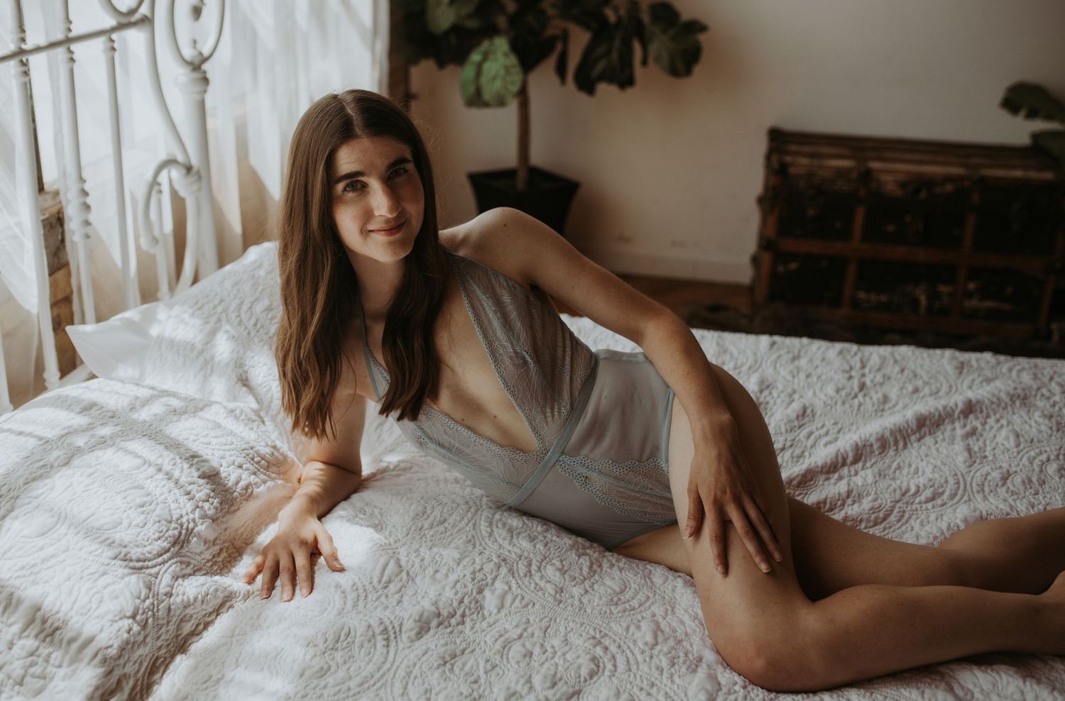 A woman in blue lingerie poses on laying down on a bed in the Grand Rapids, Michigan boudoir studio.