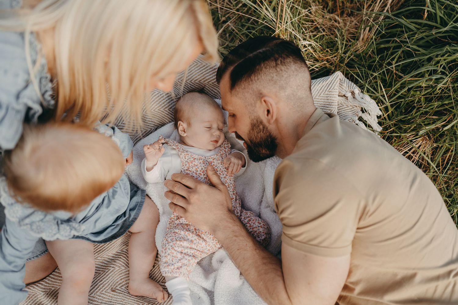 Intimate family moment captured on blanket in grassy field.