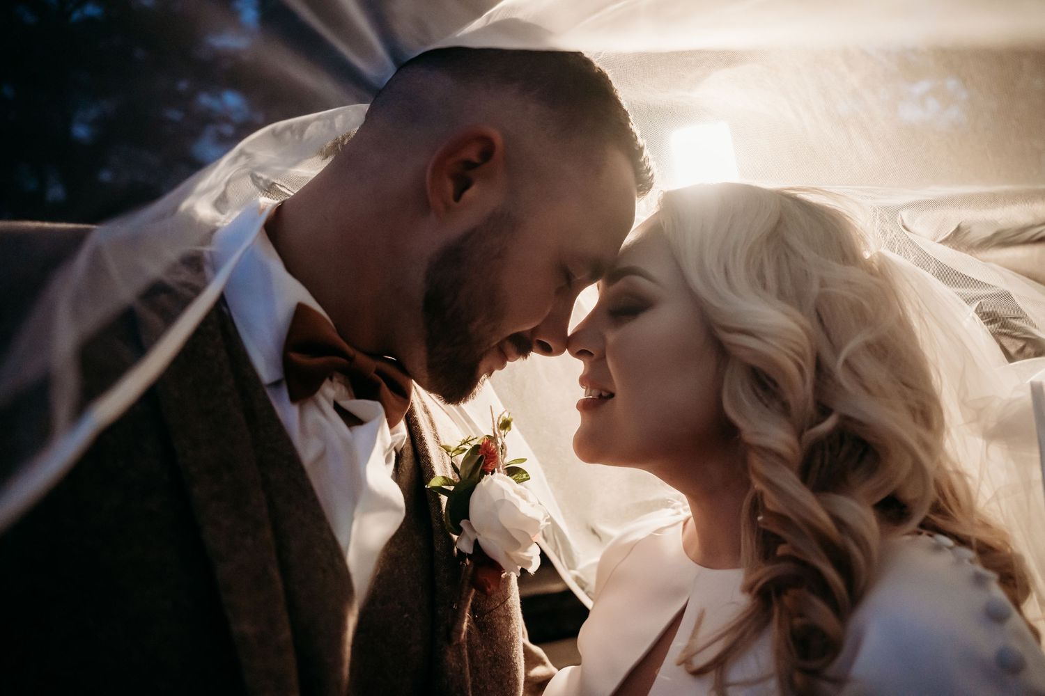 Intimate wedding portrait with couple sharing tender moment under veil.