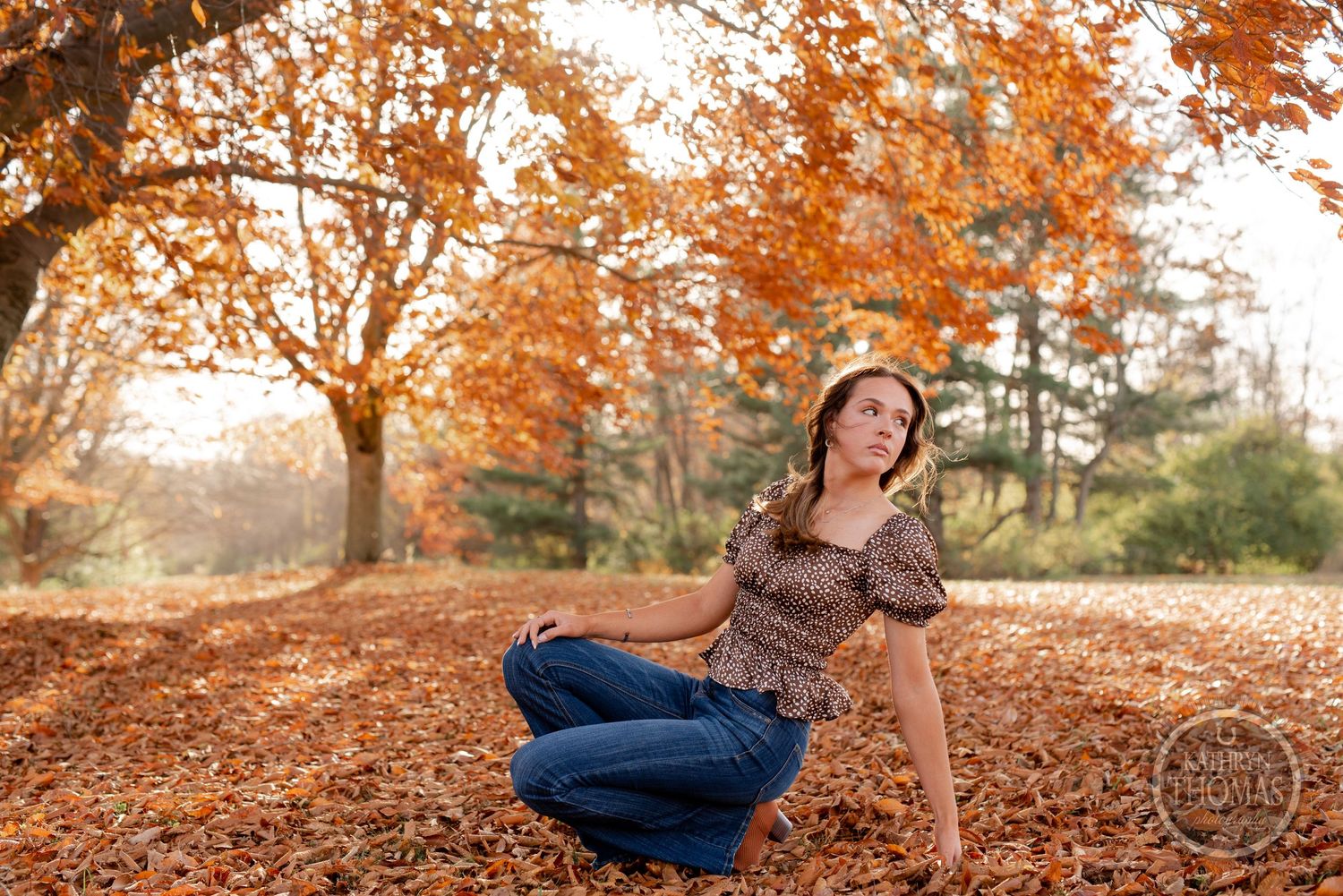 A casual outdoor portrait sitting among fallen autumn leaves wearing a patterned top.