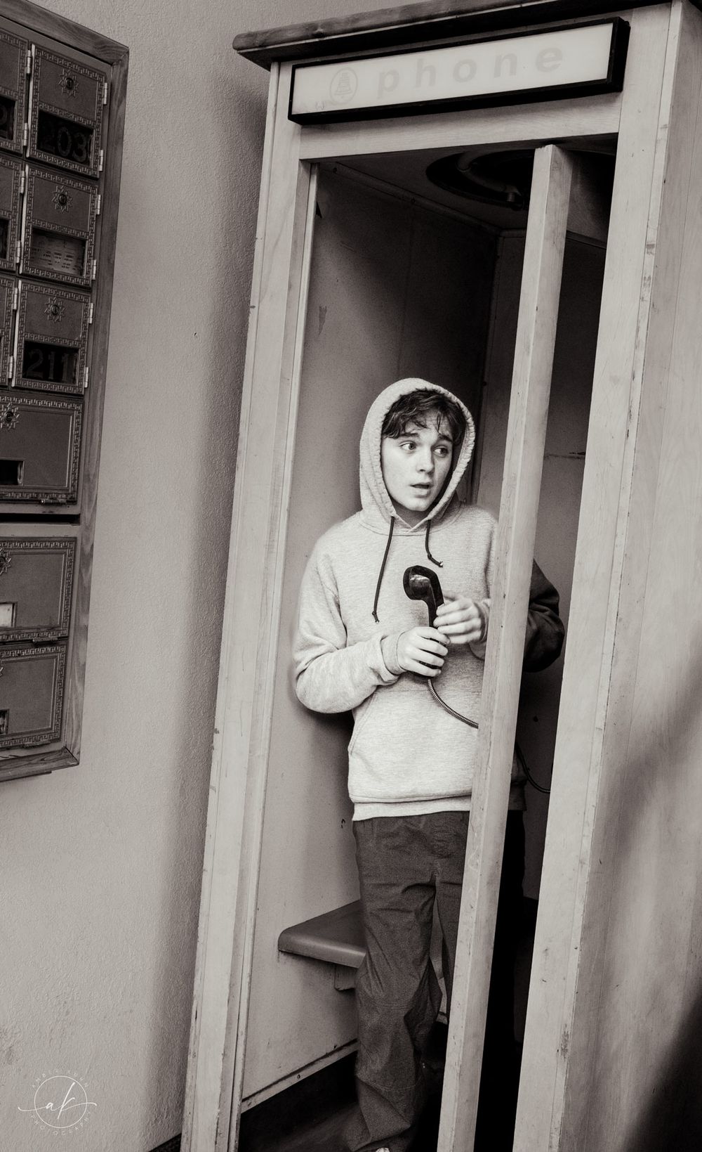 Black and white photo of hooded figure standing in narrow doorway.