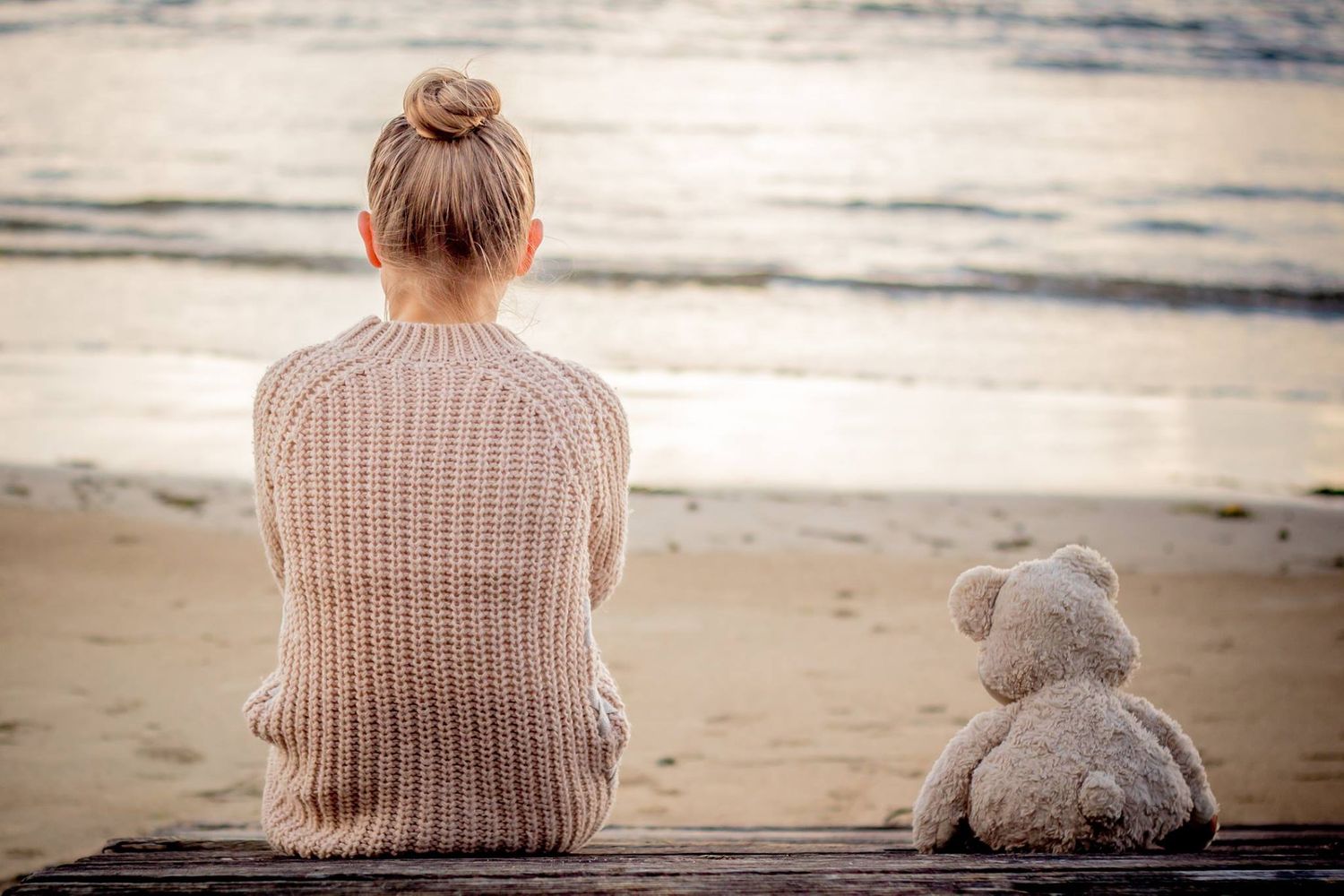 Child sitting on beach with teddy bear during family session with natural, storytelling style