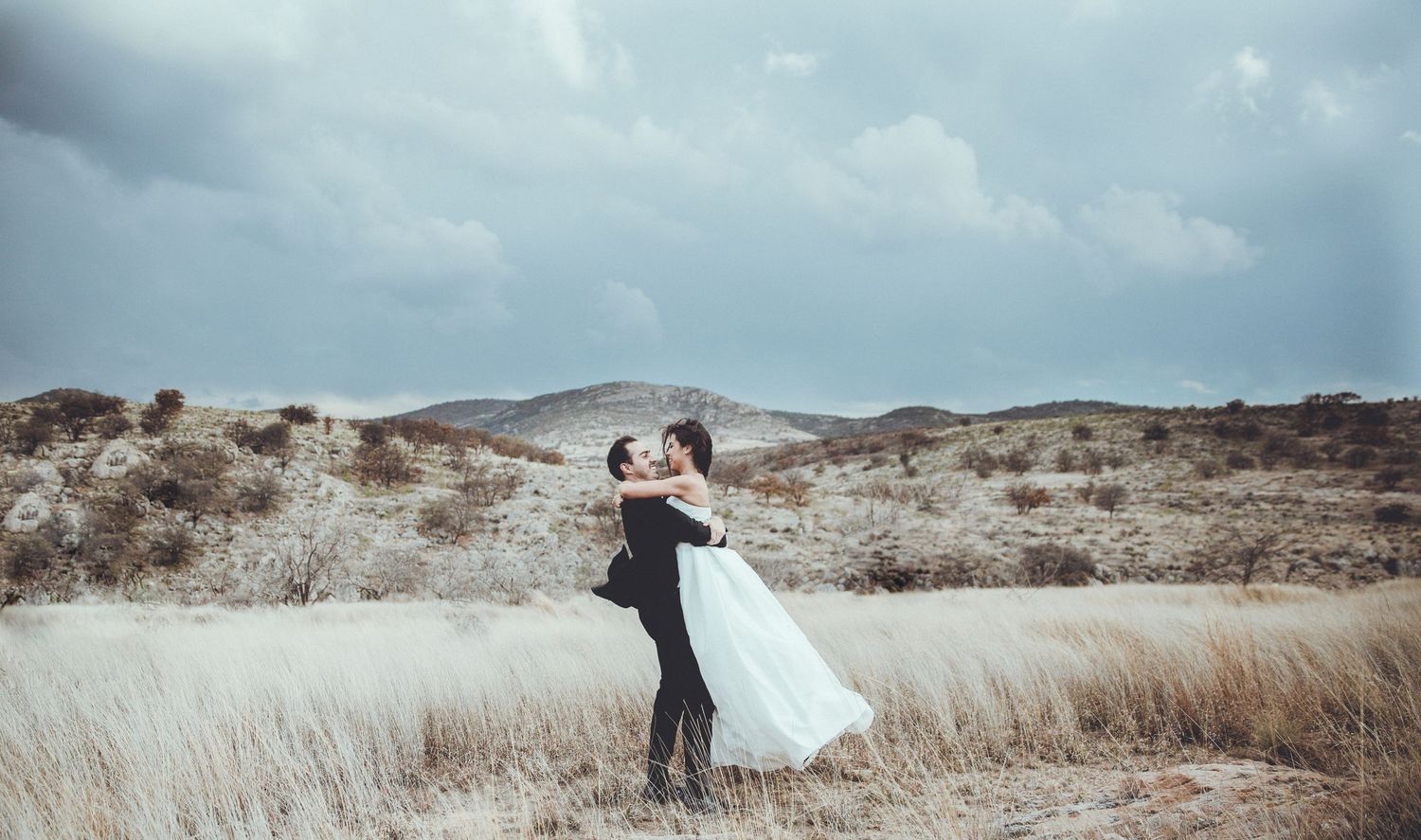 A romantic wedding pose in a windswept field with rolling hills in the background.