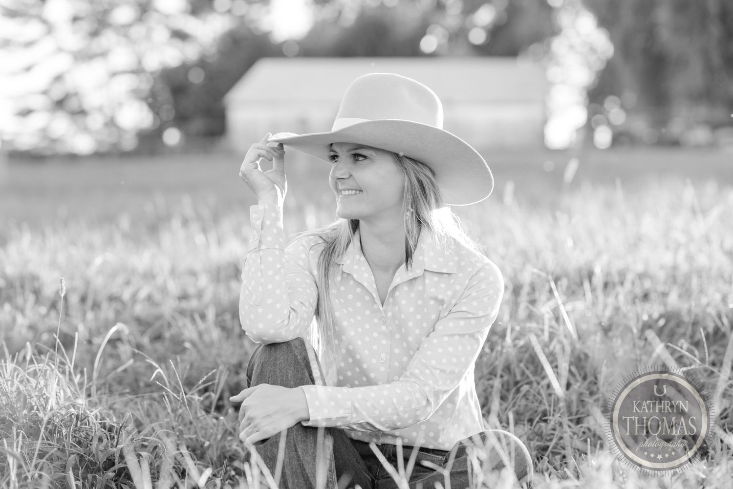 A black and white portrait of someone in western wear sitting in tall grass.