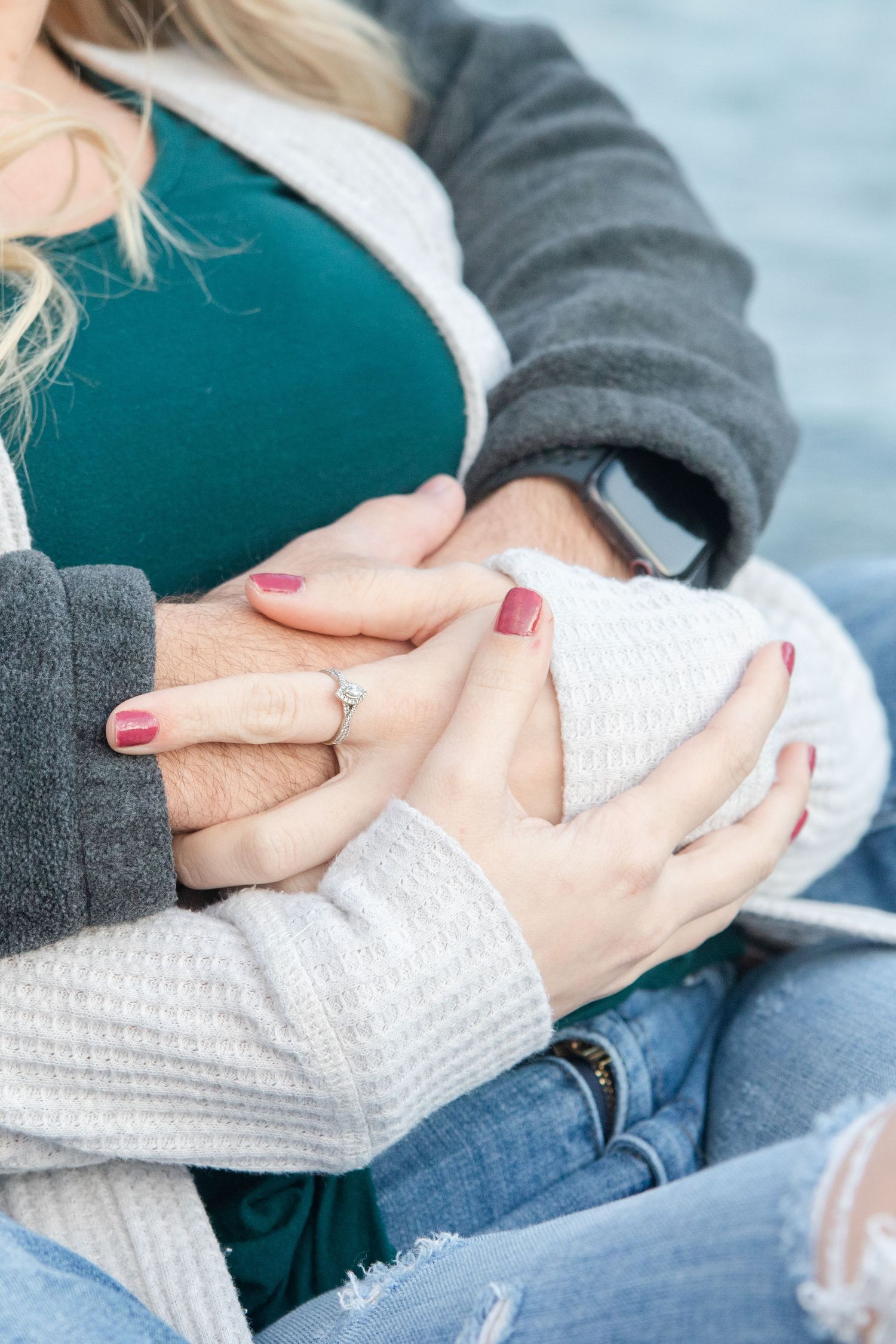 Close-up of hands with an engagement ring, wearing cozy sweaters in white and grey.