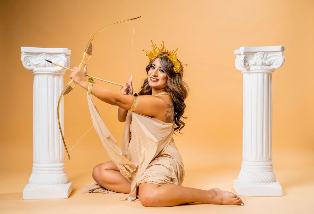 Artistic portrait with golden crown and bow against classical pillars in studio setting.