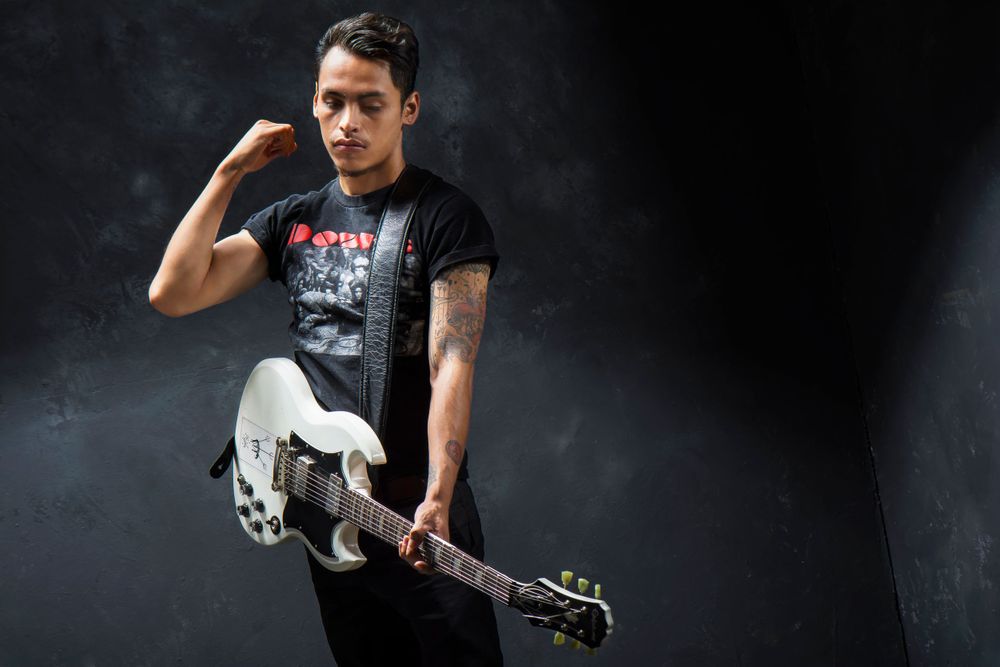 Musician in black t-shirt holding white electric guitar against dark background.