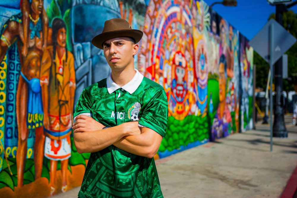 Person in green shirt and hat poses in front of colorful street art mural.