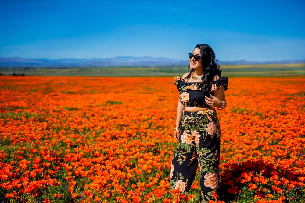 Person standing in a vibrant field of orange poppies under bright blue sky.