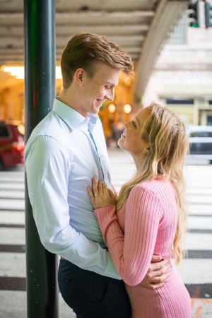 Romantic couple embracing and smiling at each other near a street pole in an urban setting.