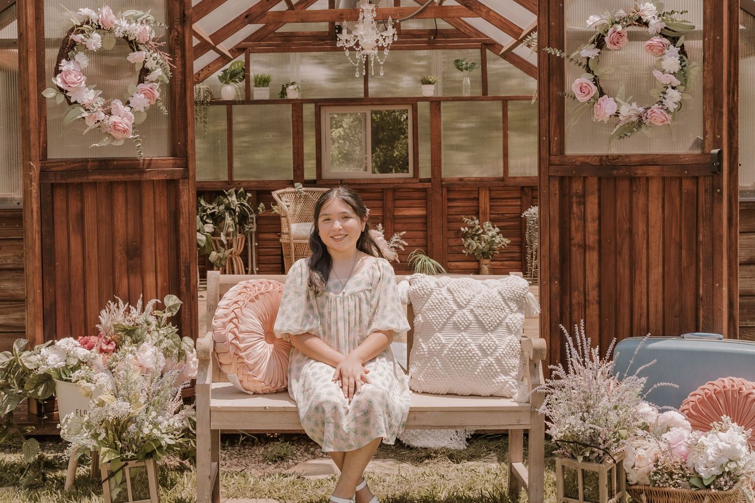 Rustic wooden garden house interior decorated with floral wreaths and pink cushioned seating.