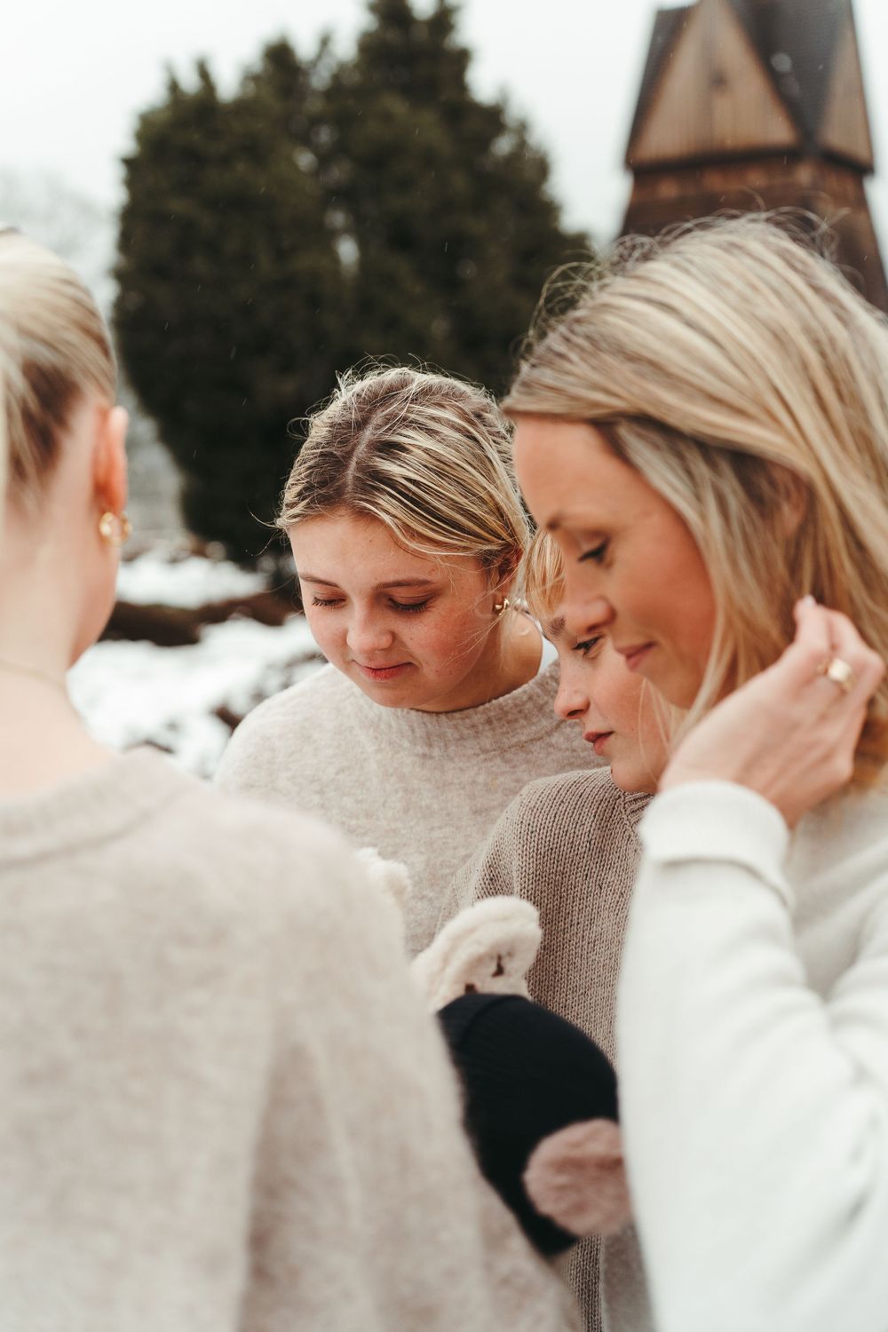 People in light-colored sweaters gather intimately outdoors with a snowy church spire in the background.