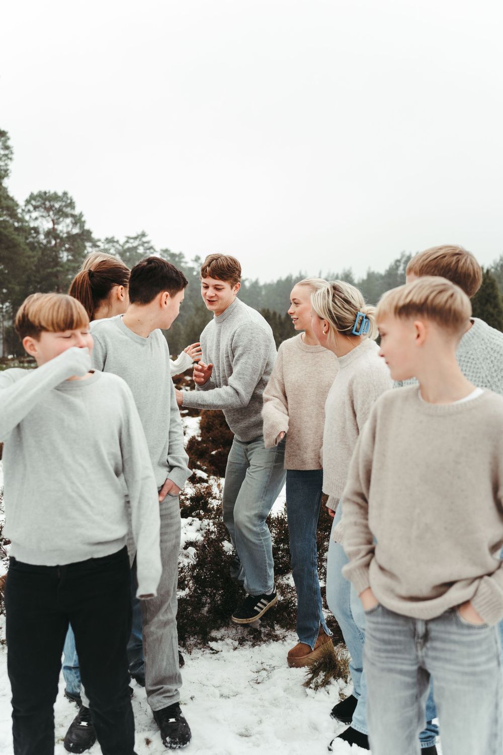 A group of people gathered together outdoors in cozy sweaters on a snowy winter day.