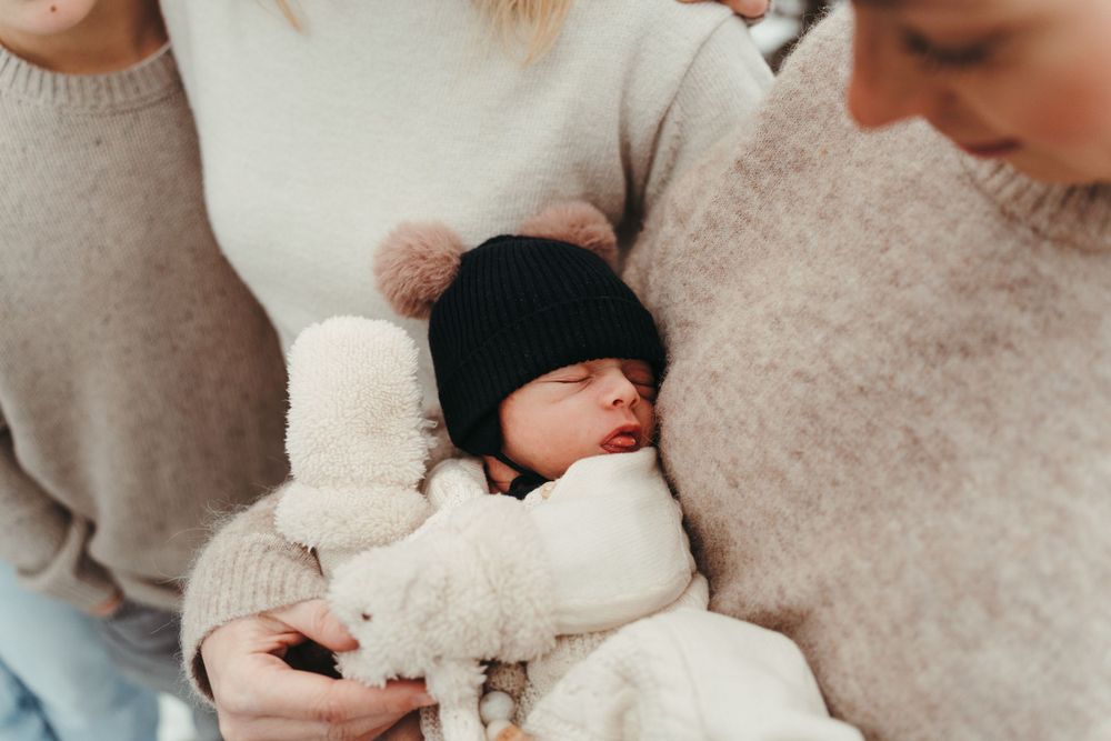 Close-up of a sleeping baby bundled in winter clothes being held by people in cozy sweaters.