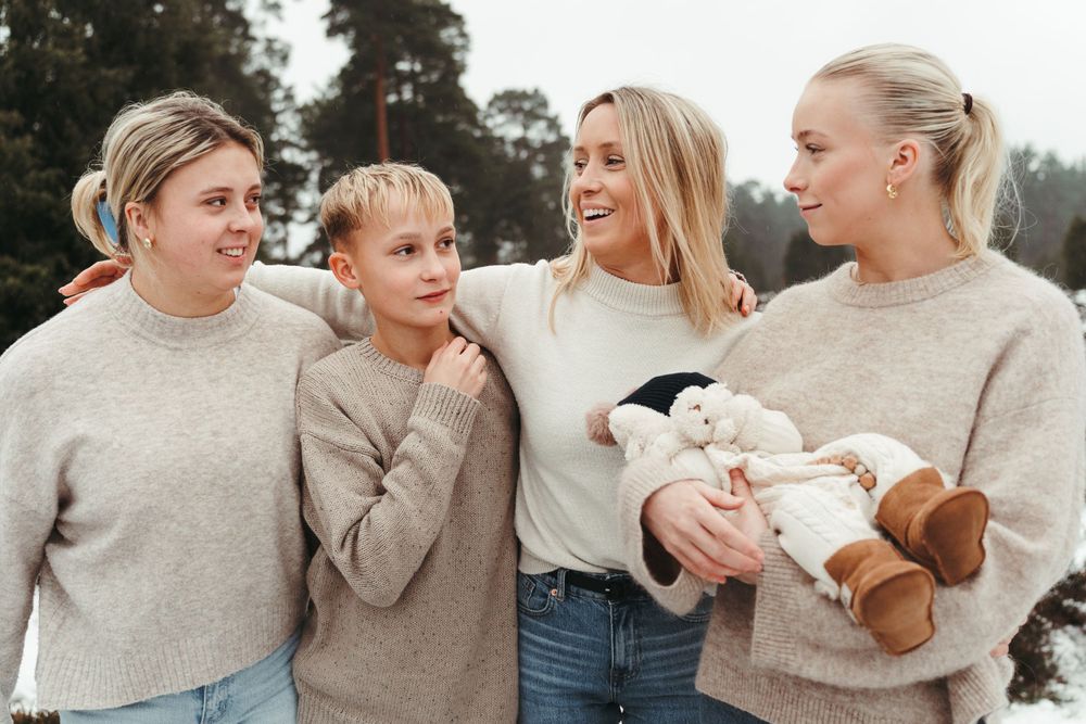 A group wearing coordinated beige sweaters poses together while holding a baby.
