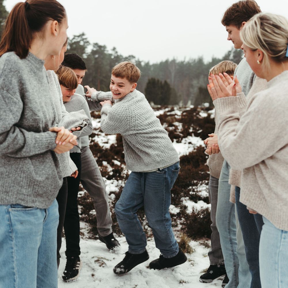 Friends laughing and having fun in the snow while wearing warm winter sweaters.