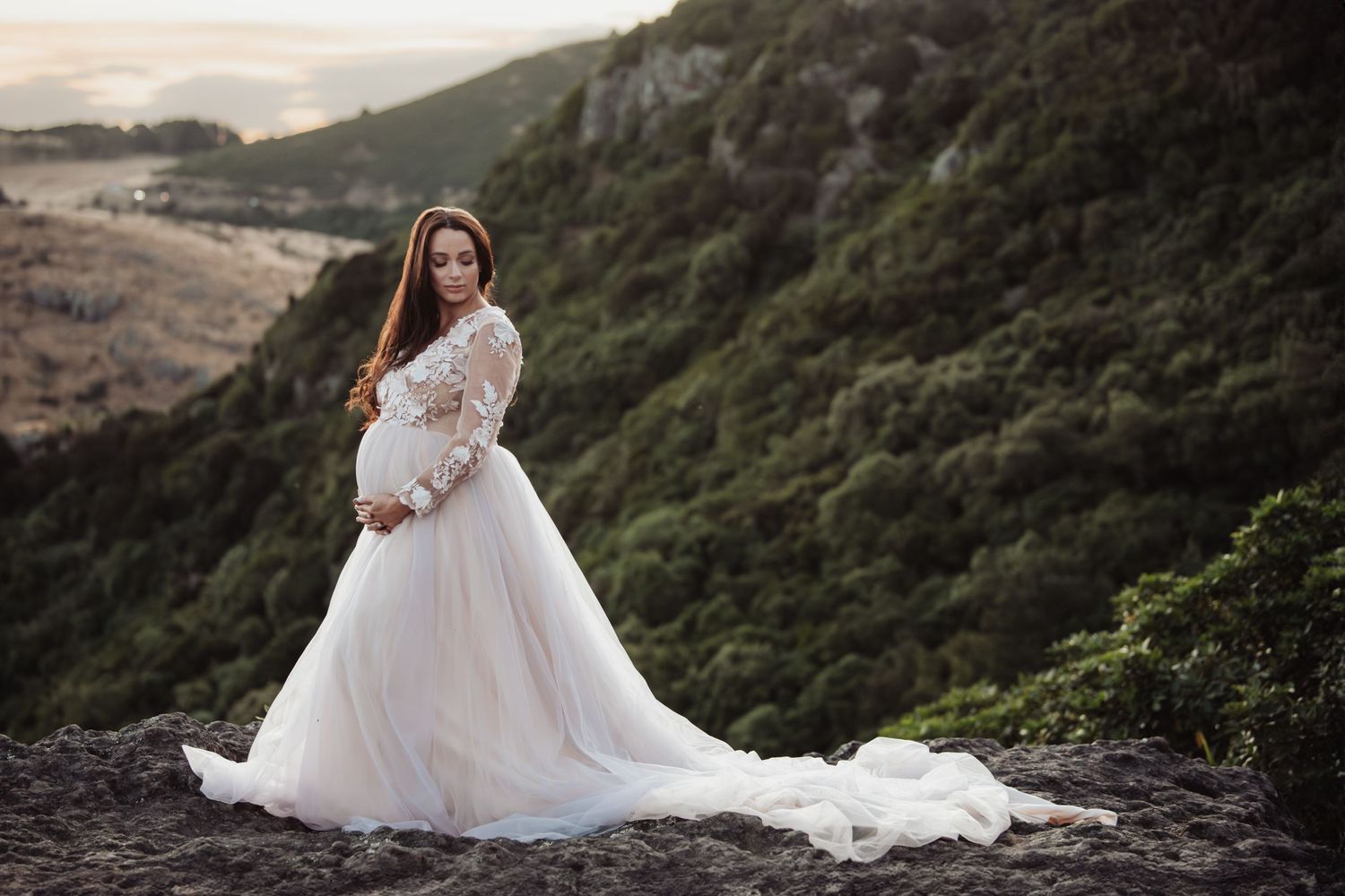 A traditional white wedding dress flows elegantly against a dramatic mountain backdrop.