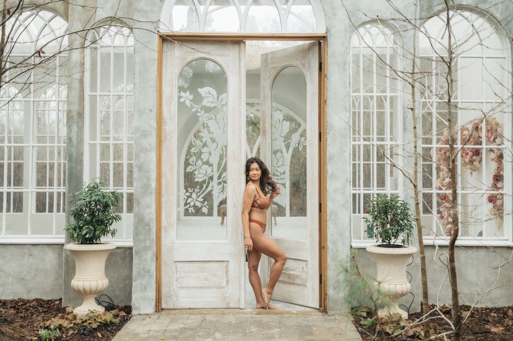 Artistic photo of a person posing in lingerie at the entrance of an elegant conservatory with arched windows.