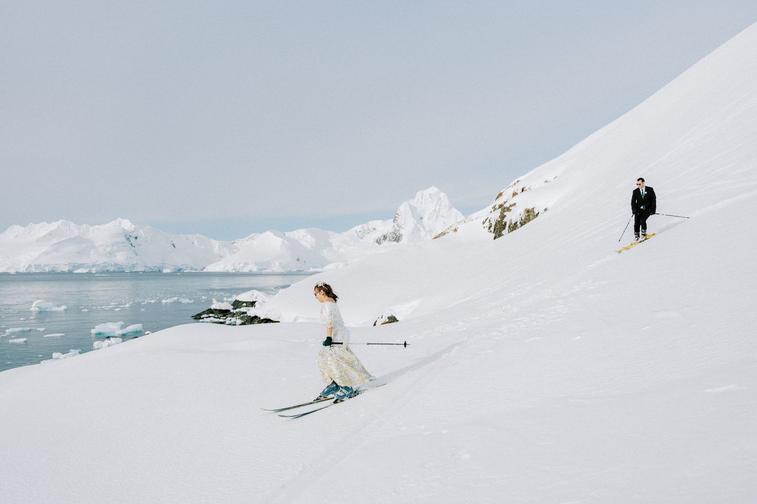 Skiers traverse a snowy slope with icebergs and glaciers in the background of a pristine polar landscape.