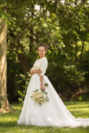 Beautiful white wedding gown with long train displayed in a sunny outdoor garden setting.