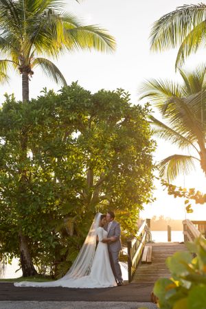 A romantic sunset wedding moment under palm trees on a tropical boardwalk.