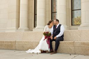 A wedding couple sits together on stone steps of a grand building.