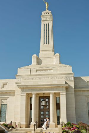 A white stone temple with tall spire stands against bright blue sky.