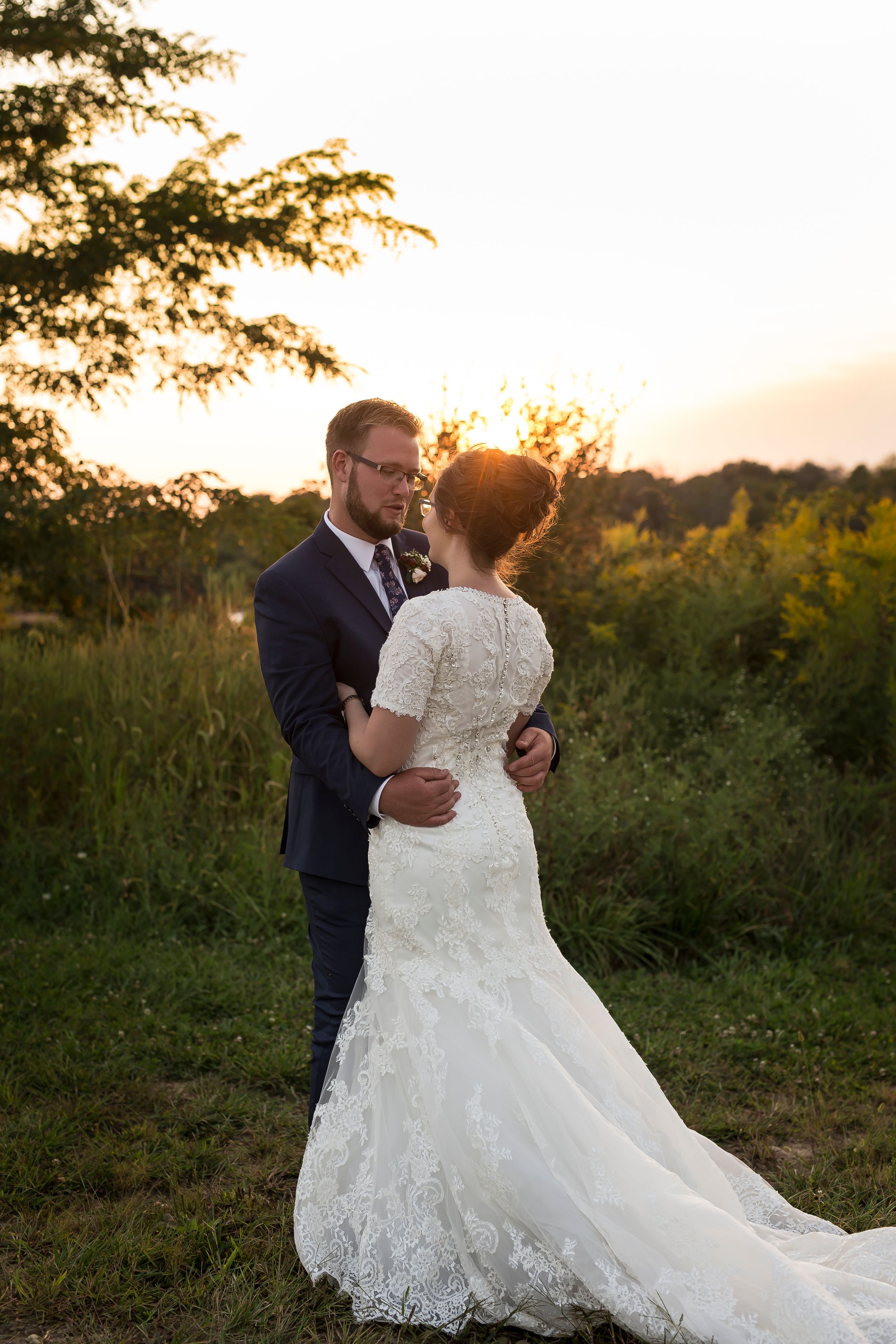 Elegant wedding couple embracing during golden hour in a rustic outdoor setting.