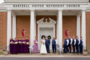 A wedding party poses on church steps with bridesmaids in purple and groomsmen in navy.