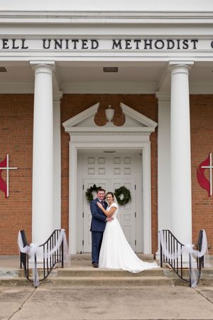A wedding couple stands in front of the white columns and brick facade of Hartzell United Methodist Church.