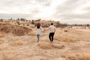 couple holding hands while skipping away together through a wide golden field framed by rolling hills and soft light