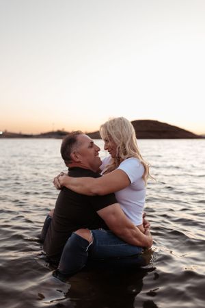 couple embracing in the shallow lake water at sunset, smiling at each other as warm golden light reflects off the waves and hills