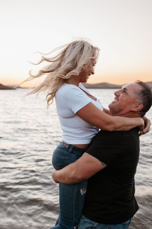 couple standing in shallow lake water at sunset, smiling and holding each other with hills in background