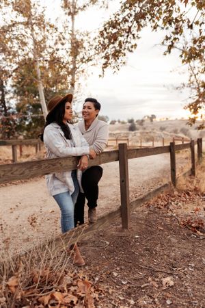 couple leaning on a wood fence surrounded by fallen leaves and trees