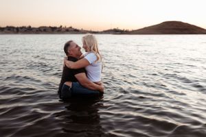 couple embracing in the shallow lake water at sunset, smiling at each other as warm golden light reflects off the waves and hills