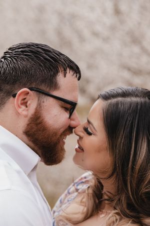 close up of a couple embracing in a almond orchard while in bloom, noses touching leaning in for a kiss