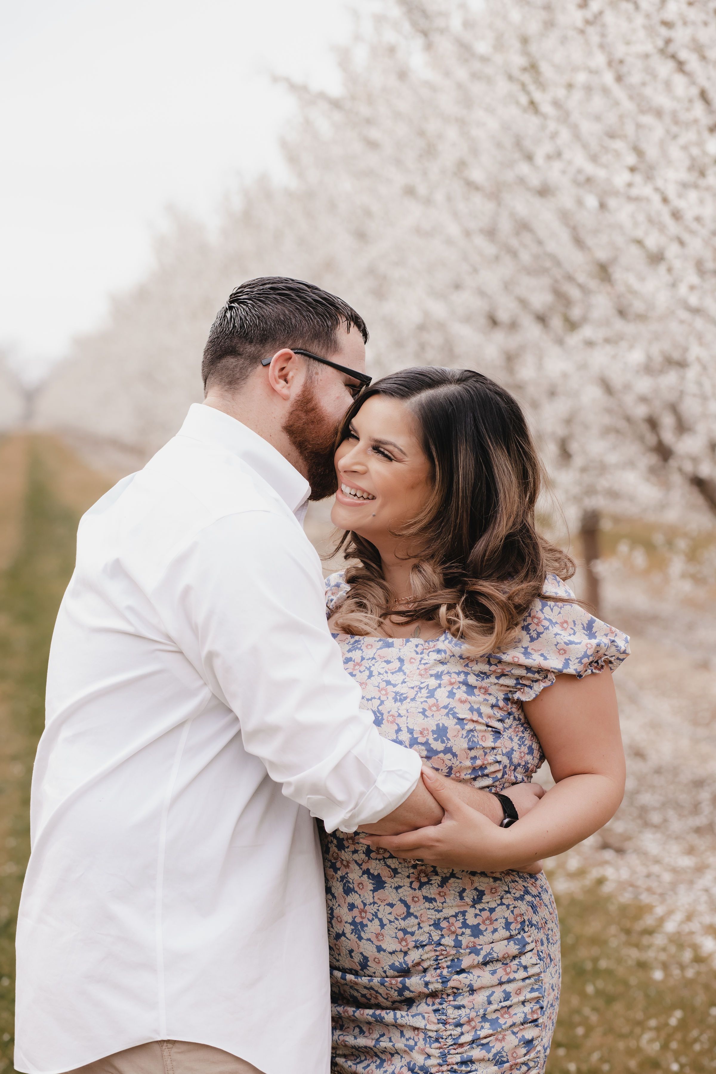 couple embracing in a almond orchard while in bloom, one partner is leaning in to the others ear
