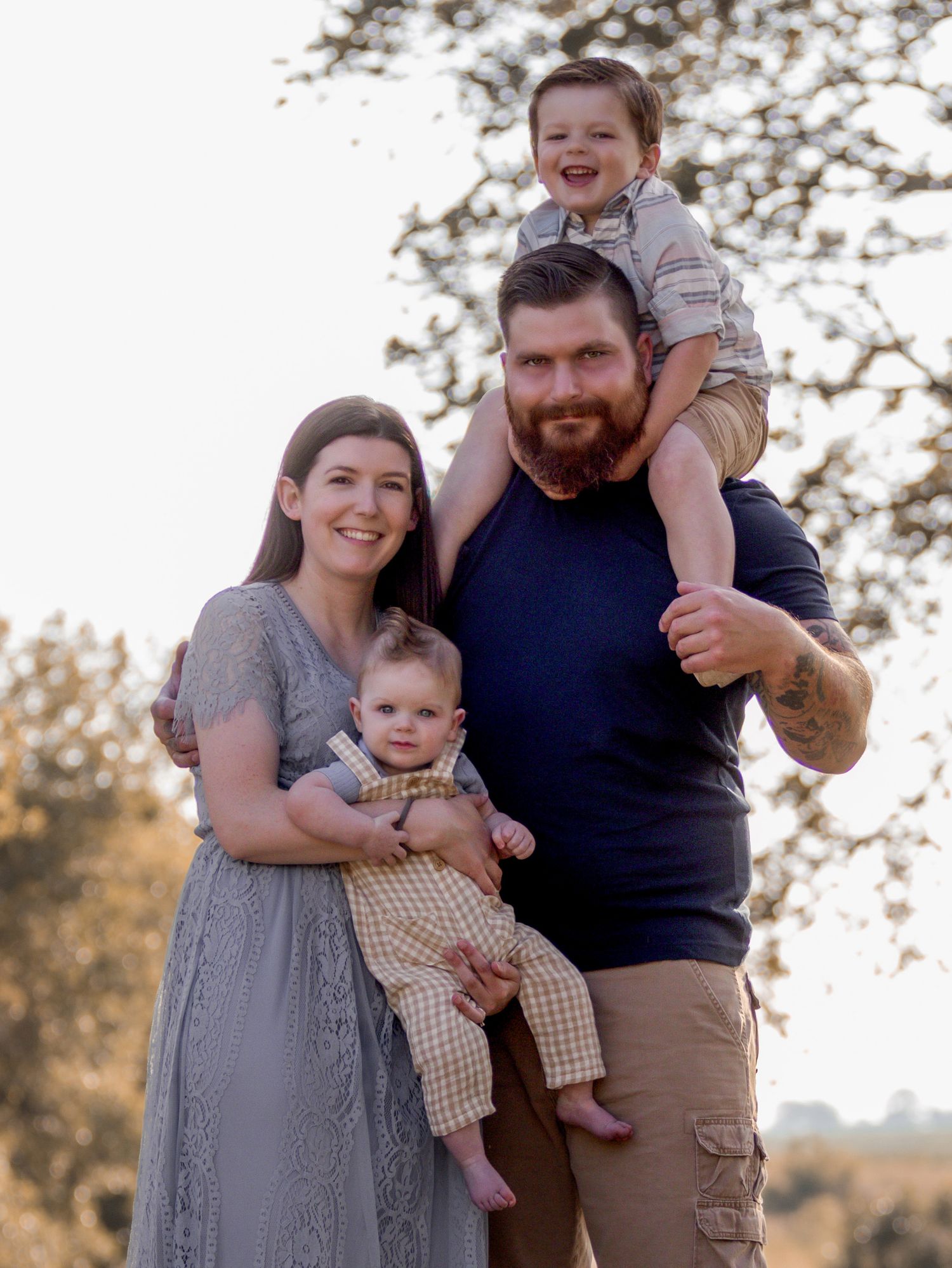 A family portrait of parents with their two young children outdoors at sunset.