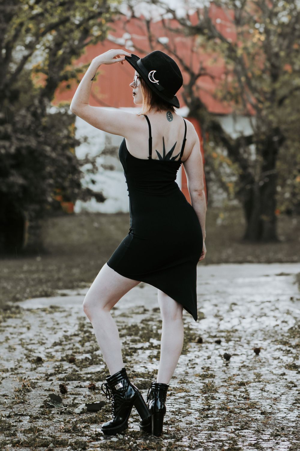 Person in black outfit and boots posed on ground covered with fallen leaves.