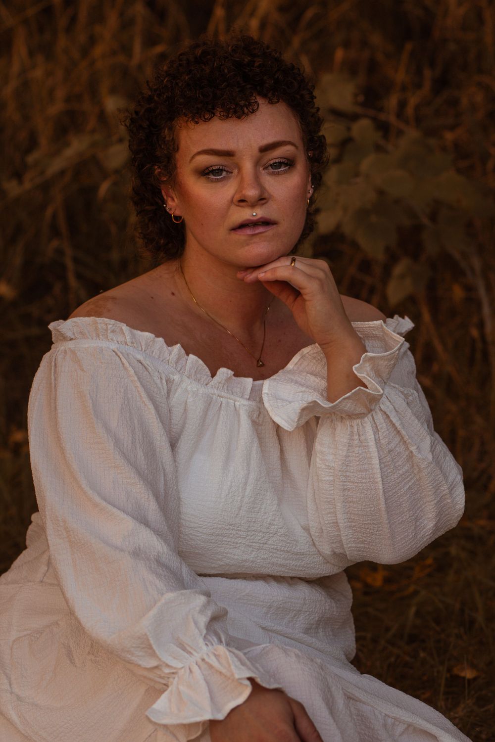 Figure in flowing white period dress with ruffled collar in atmospheric outdoor setting.