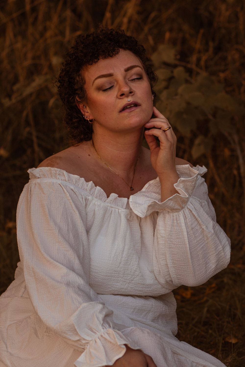 Person wearing romantic white dress with ruffled collar in moody outdoor portrait.