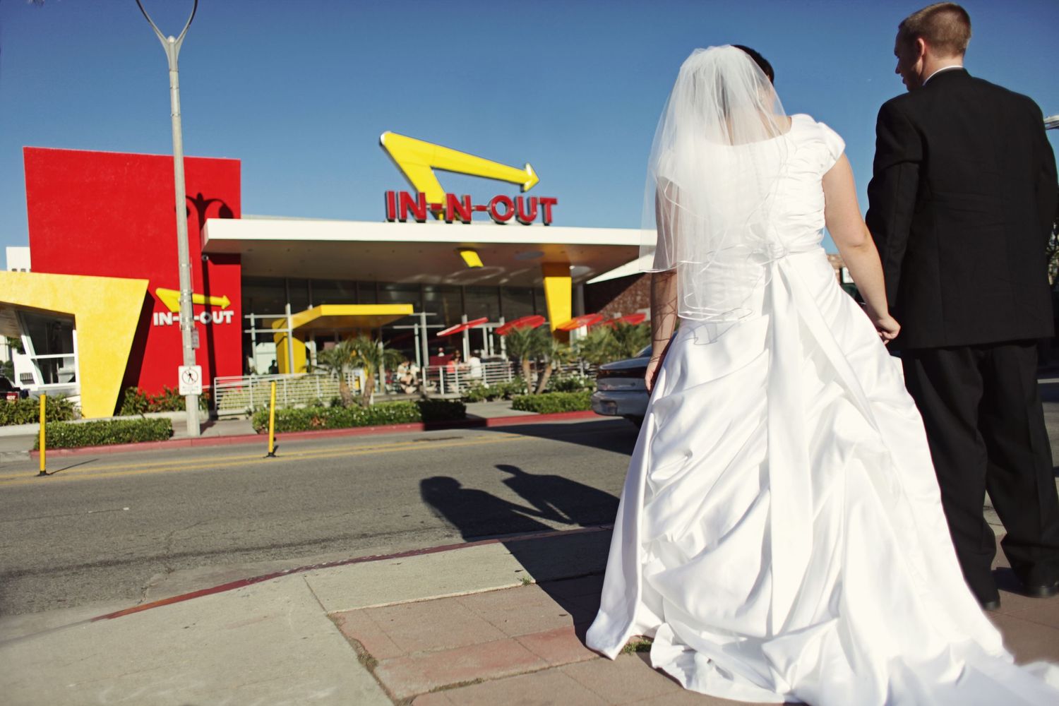 Newlywed couple walking towards retro-styled In-N-Out Burger restaurant.