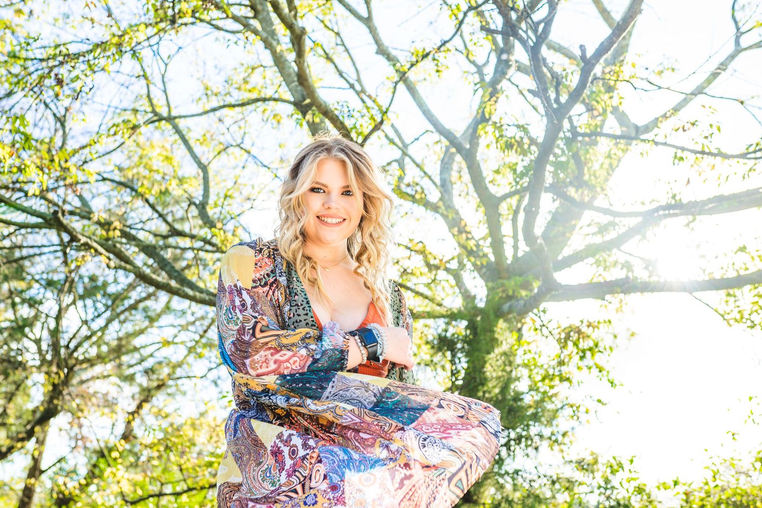 A floral dress photoshoot against sunlit trees creates a dreamy springtime portrait in nature.