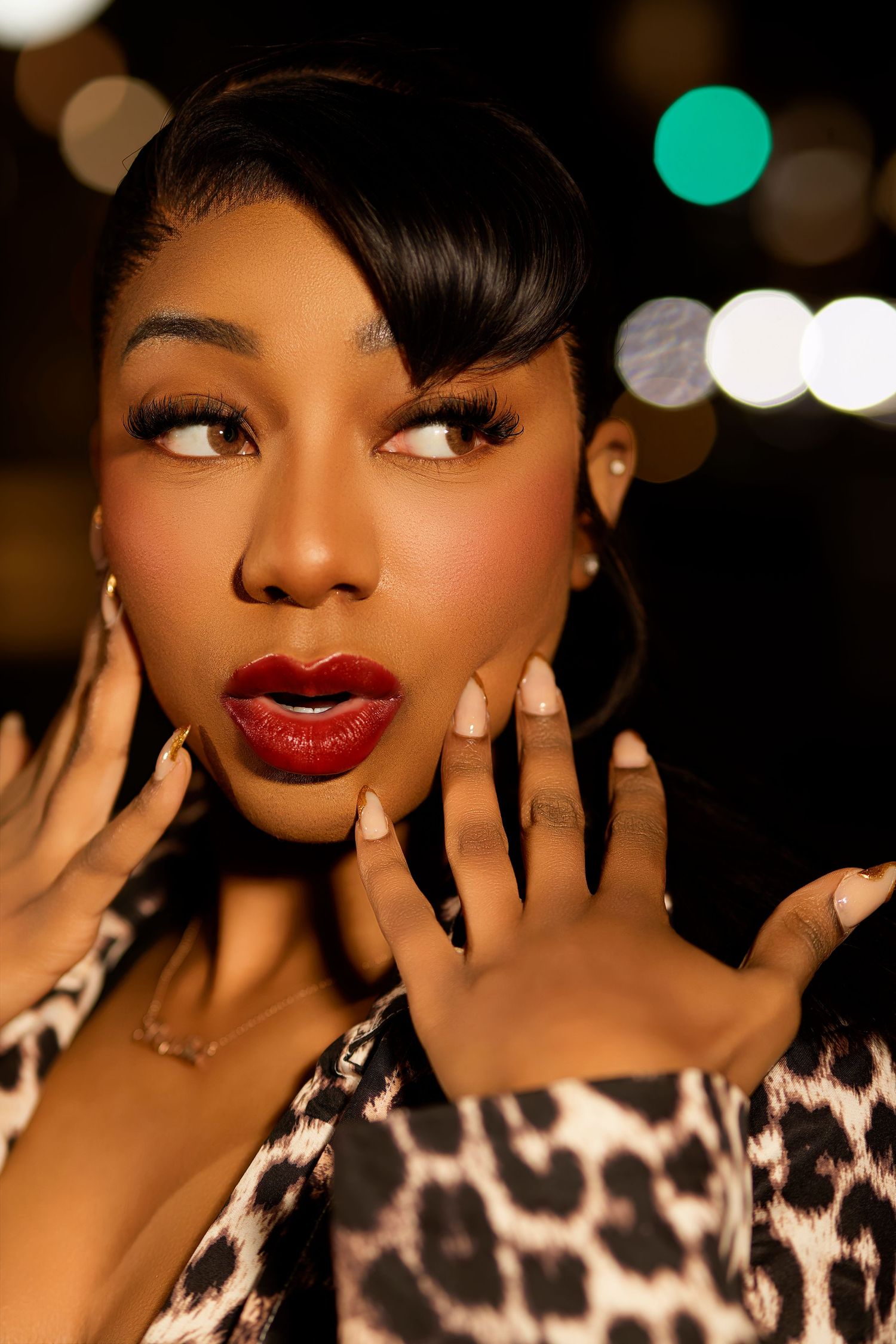 A beauty portrait showing long black hair, delicate jewelry, and glowing skin against a dark gray backdrop.