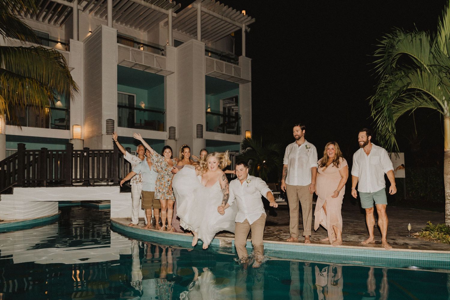 Group of friends having fun jumping into a resort swimming pool at night.