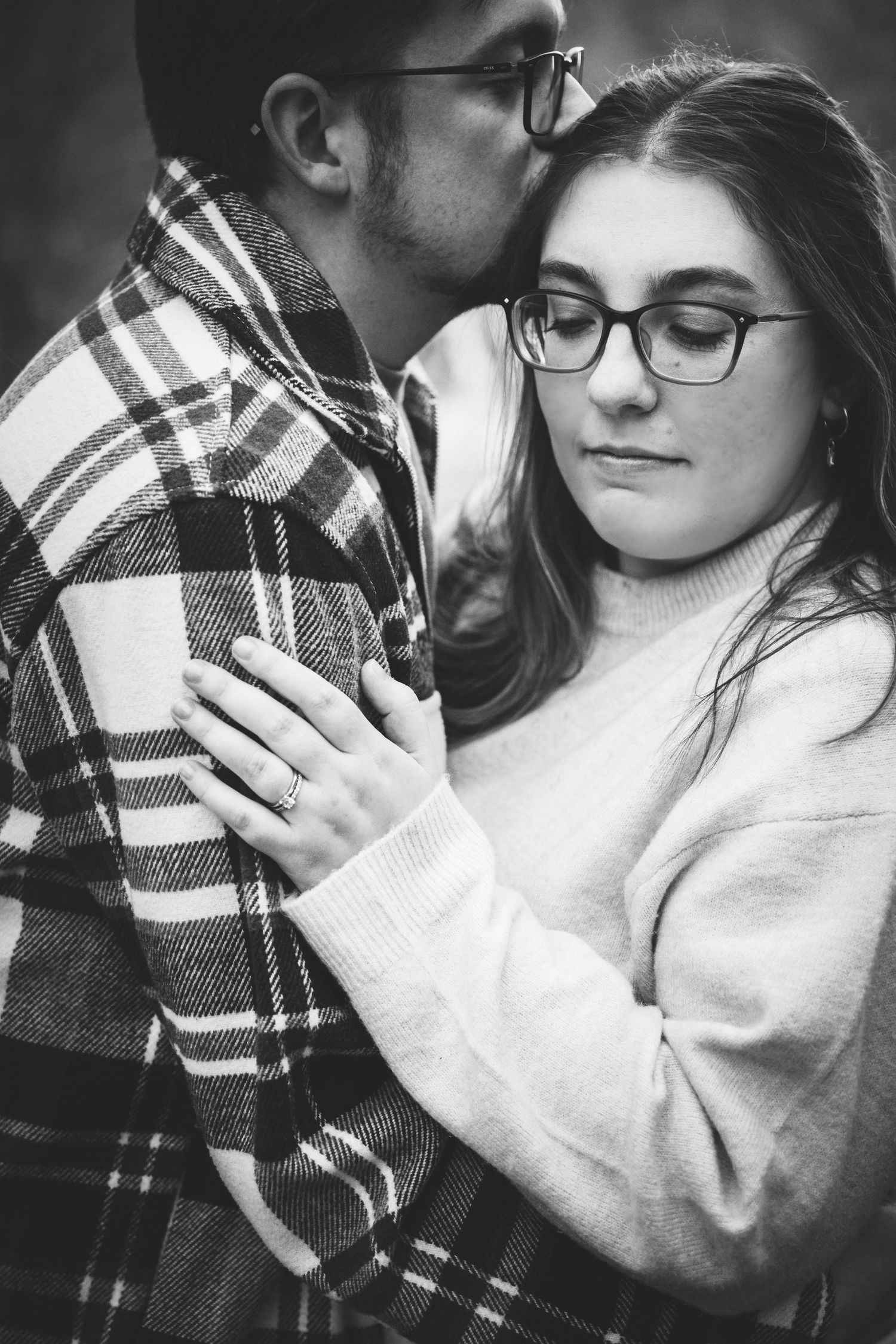 young couple embracing in cozy sweaters with detailed picture of engagement ring