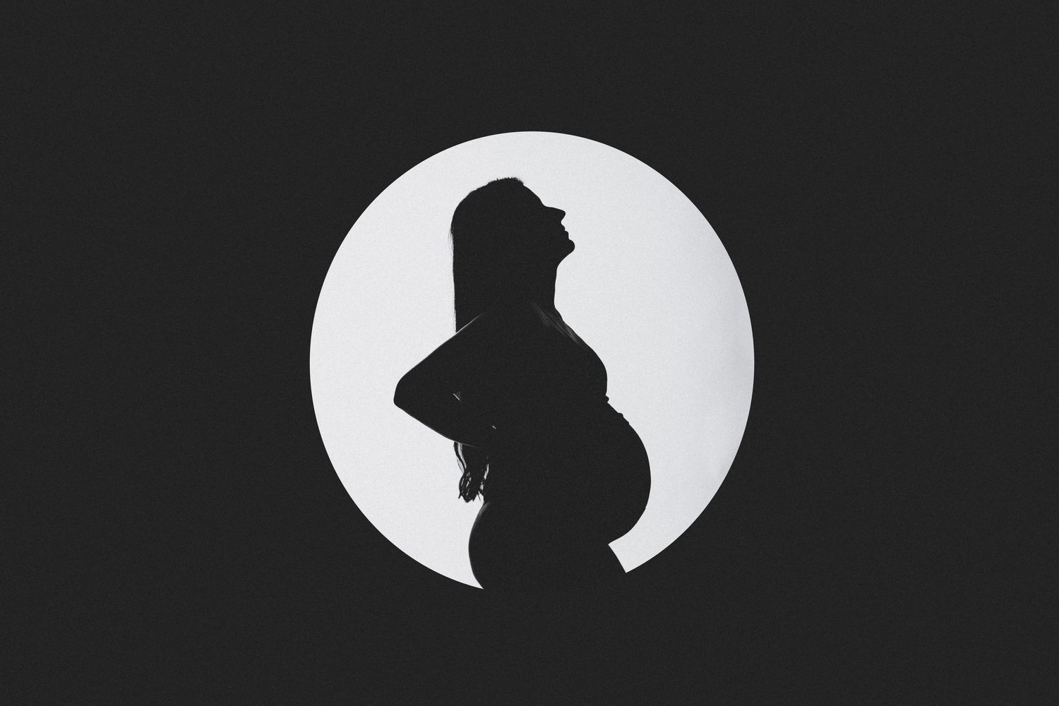 A side profile silhouette of a pregnant woman against a bright white circular background.