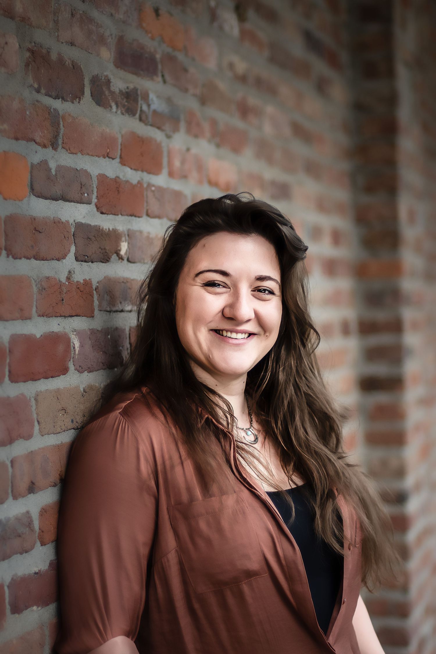 Professional headshots against a rustic brick wall background with warm lighting.